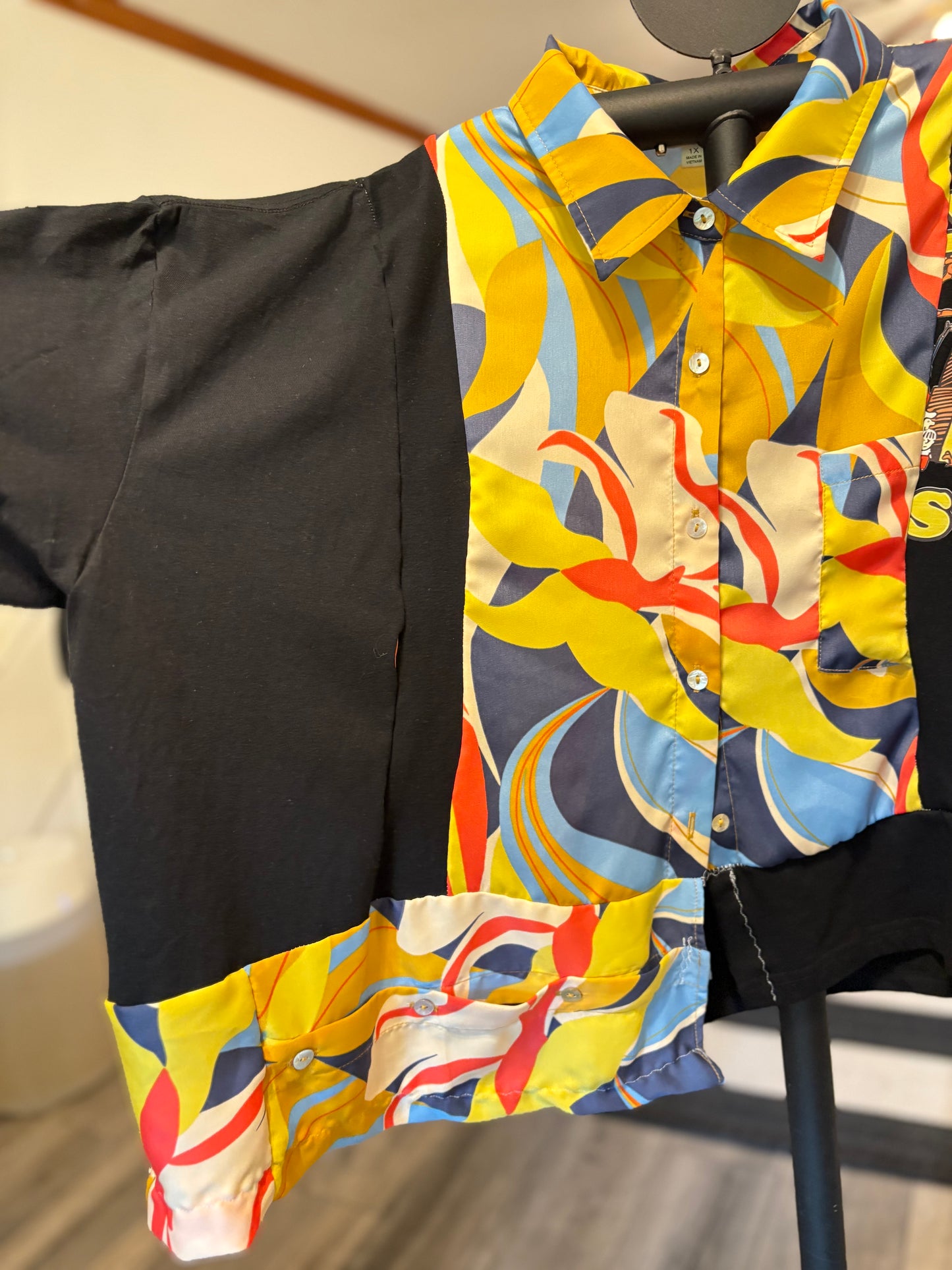 Colorful patterned short-sleeve button-up shirt with vibrant designs and contrasting black sleeves, perfect for summer style. Sleeve