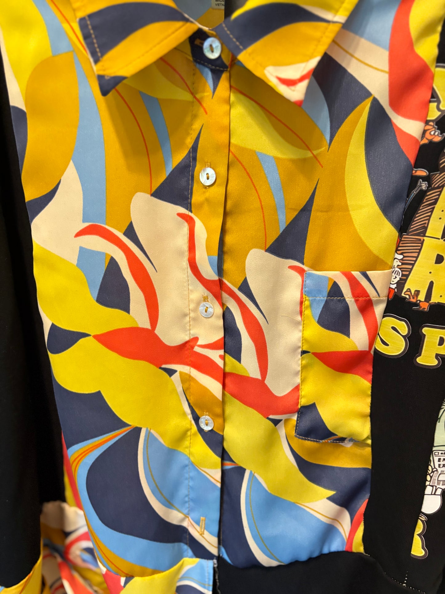 Colorful patterned short-sleeve button-up shirt with vibrant designs and contrasting black sleeves, perfect for summer style. Detail