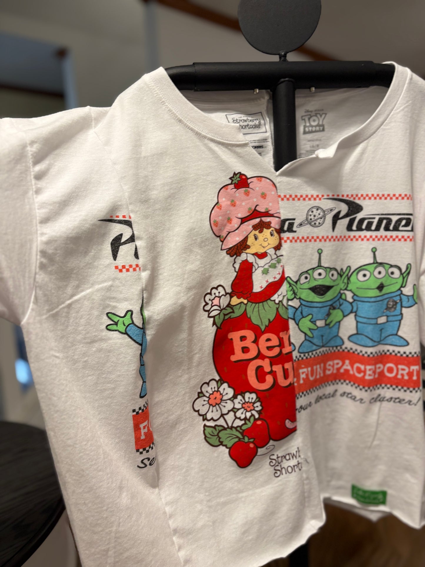 Vintage-inspired white tee featuring Strawberry Shortcake and Toy Story aliens, perfect for casual wear. Sleeve